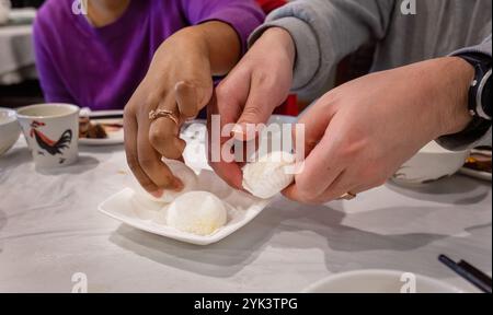 Mains de deux personnes ramassant des petits pains à dessert dans une assiette blanche dans un restaurant chinois. Banque D'Images