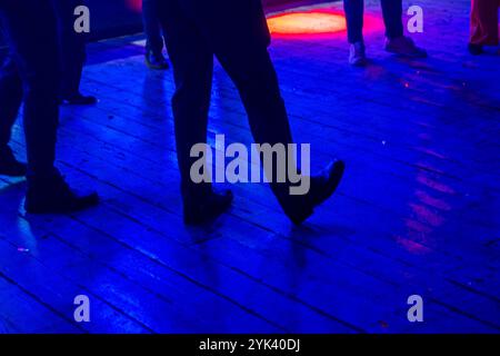 Une scène dynamique avec un éclairage coloré met en valeur les pieds en mouvement sur la piste de danse d'une boîte de nuit, capturant l'énergie vibrante de la vie nocturne. Banque D'Images