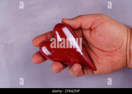 Une paire de mains tient des coeurs en porcelaine rouge sur une table en béton gris, symbolisant l'amour et la romance pour la Saint-Valentin dans une vue de haut en bas Banque D'Images