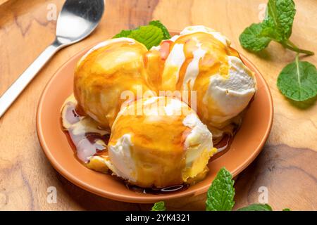 Trois boules de crème glacée à la vanille avec garniture de caramel et feuilles de menthe verte fraîche sur l'assiette sur la table en bois. Banque D'Images