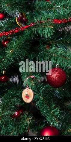 Sapin de Noël décoré de façon festive avec des ornements rouges et un ornement en bois fait à la main, capturant l'esprit des fêtes et la chaleur saisonnière. Banque D'Images