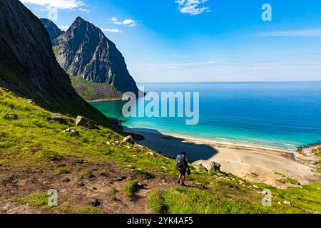 Un randonneur sur le sentier de la plage de Kvalvika dans les Lofoten, en Norvège, entouré de falaises accidentées et de superbes vues côtières lors d'une journée d'été parfaite Banque D'Images