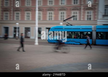 Tram bleu passant par la rue de la ville avec piétons flous et cyclistes Banque D'Images