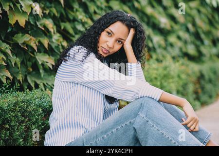 Un portrait décontracté mettant en vedette une jeune femme avec de beaux cheveux bouclés entourée par la nature Banque D'Images