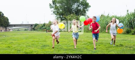 Les enfants avec des ballons courent dans le parc d'été Banque D'Images