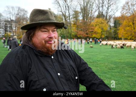 Nuremberg, Allemagne. 17 novembre 2024. Le berger Thomas Gackstatter se tient sur la Wöhrder Wiese. Ses moutons peuvent être vus en arrière-plan. Le berger Thomas Gackstatter, ses enfants et ses assistants emmènent environ 700 moutons à travers le centre-ville de Nuremberg pour amener les animaux dans leurs pâturages d'hiver. Crédit : Daniel Vogl/dpa/Alamy Live News Banque D'Images