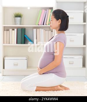 Femme calme méditant à la maison yoga prénatal. Pleine longueur saine 8 mois enceinte calme femme asiatique méditant à la maison. Posture du héros de yoga de relaxation. Copyri Banque D'Images