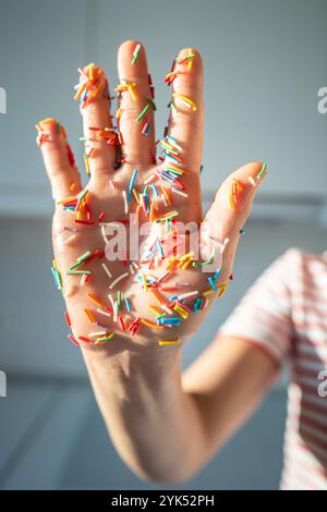 Main de femme recouverte de saupoudres de sucre colorées pour garnir la boulangerie, décorations de cuisson colorées. Banque D'Images