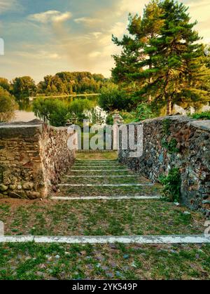 Village médiéval italien, Castellaro Lagusello près de Mantoue. Un escalier en pierre descend vers un lac serein entouré de verdure. Banque D'Images