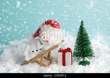 Bonhomme de neige est relaxant sur la chaise longue. veille de noël noel. il est temps de se détendre. Bonhomme de neige, arbre de Noël et boîte cadeau sur fond bleu. Concept de vacances d'hiver Banque D'Images