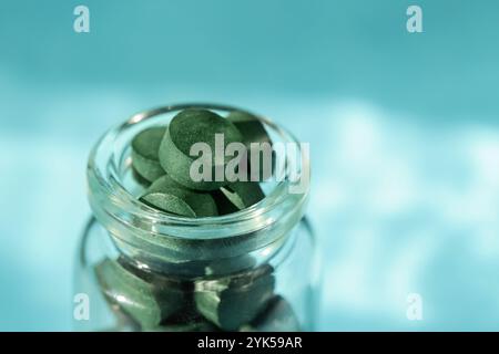 Pilules de spiruline dans une bouteille en verre sur fond bleu. Nutrition antioxydante. Copier l'espace Banque D'Images