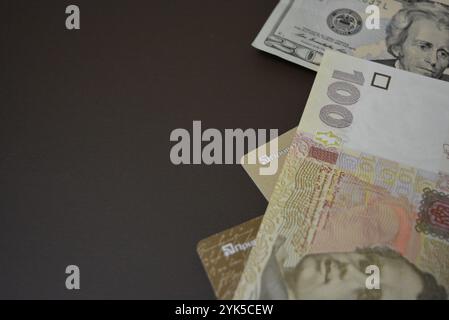 Économie, finance, littératie financière, commerce. 20 dollars américains, 100 hryvnias ukrainiens sous forme de papier et cartes bancaires en plastique or sont sur un mat brun. Banque D'Images