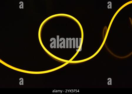 De beaux fils jaunes et orange épais sont chaotiquement situés et tordus sur un fond en plastique noir. Câble électroluminescent, tubes néon. Banque D'Images
