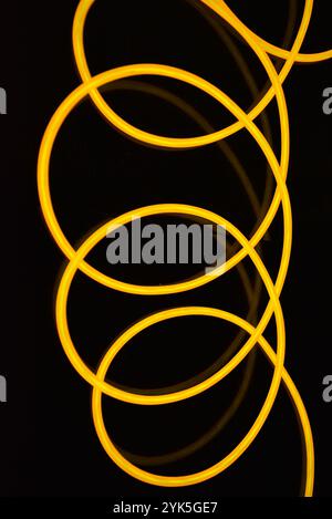 De beaux fils jaunes et orange épais sont chaotiquement situés et tordus sur un fond en plastique noir. Câble électroluminescent, tubes néon. Banque D'Images