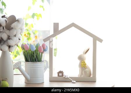Clé et minuscule maison de maison confortable avec décor de Pâques avec lapin et oeufs sur la table de la cuisine. Bâtiment, conception, projet, déménagement à la nouvelle maison, hypothèque, Banque D'Images