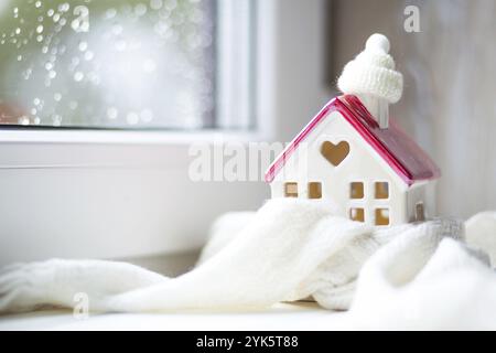 Maison confortable est enveloppé dans un chapeau et une écharpe dans un décor de rebord de fenêtre-tempête de neige. Hiver, neige, isolation de la maison, protection contre le froid et les intempéries, pièce Banque D'Images