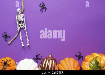 Halloween mise en page d'une guirlande de squelette sur une corde, lueur Jack o Lantern, citrouilles, araignées sur un fond violet. Flat Lay horreur et un terrible ho Banque D'Images
