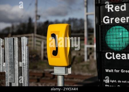 Boîte téléphonique jaune pour un dispositif de contrôle de passage à niveau, avec lumière verte pour les piétons. En arrière-plan, un paysage flou est visible Banque D'Images