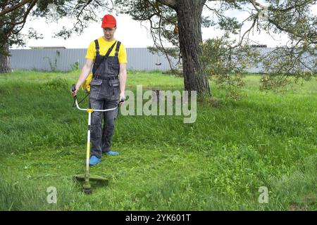 Un jardinier masculin tond l'herbe verte de la pelouse dans l'arrière-cour avec une tondeuse à essence. Tondeuse pour le soin d'un terrain de jardin Banque D'Images