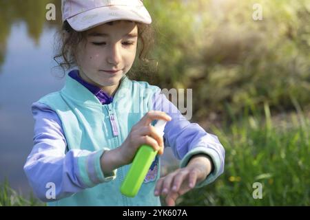 Une fille pulvérise des moustiques sur la peau dans la nature qui mord ses mains et ses pieds.Protection contre les piqûres d'insectes, répulsif sans danger pour les enfants.recr. Extérieure Banque D'Images