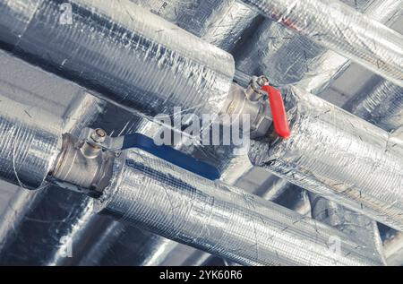 Dans un environnement industriel, deux commandes de vannes rouges et bleues sont positionnées sur des tuyaux métalliques isolés, mettant en valeur les caractéristiques essentielles de la plomberie. Banque D'Images