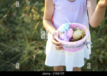 Jolie fille drôle avec des oeufs de Pâques peints au printemps dans la nature dans un champ avec lumière du soleil dorée et des fleurs.Vacances de Pâques, lapin de Pâques avec oreilles, colo Banque D'Images