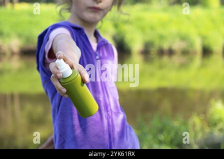 Une fille pulvérise des moustiques sur la peau dans la nature qui mord ses mains et ses pieds.Protection contre les piqûres d'insectes, répulsif sans danger pour les enfants.recr. Extérieure Banque D'Images