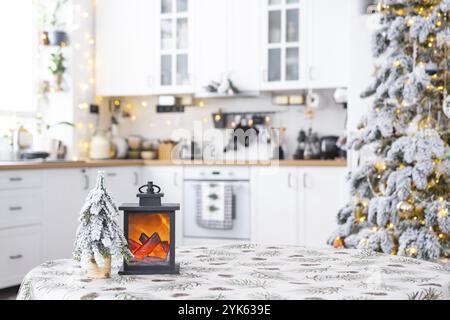 Décor de Noël festif sur une table ronde vide avec nappe avec aiguilles de pin et cônes imprimés dans une cuisine blanche, intérieur moderne avec un tr de Noël Banque D'Images