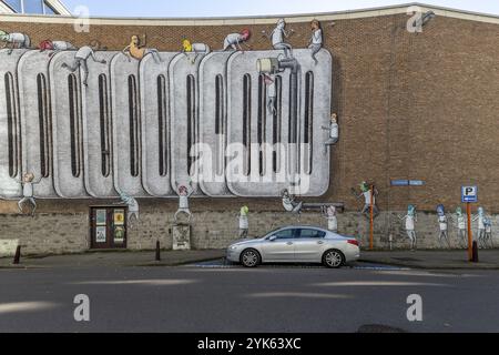 Grand graffiti mural sur le mur de briques des bâtiments de la rue Craenendonck derrière une voiture argentée garée, Louvain, Flandre, Brabant flamand, Belgique, euro Banque D'Images