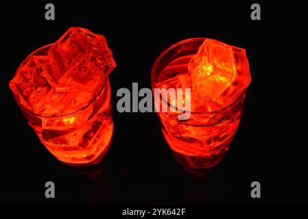 Des glaçons rouges brillants flottent dans des verres à champagne avec une boisson. Les objets en plastique fabriqués sous forme de glaçons avec une diode intégrée s'illuminent. Banque D'Images