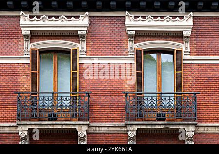 Deux balcons symétriques avec volets en bois ornent une façade en briques vintage. Banque D'Images