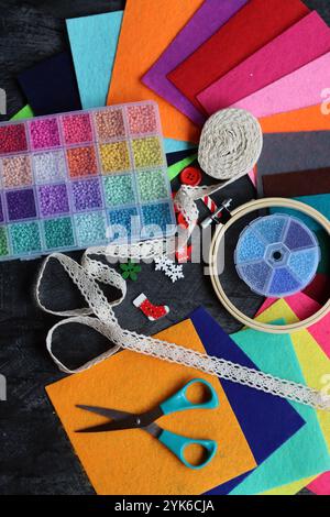 Projet DIY en fabrication. Photo vue de dessus de perles de verre colorées, tissu feutre et ciseaux sur le bureau gris foncé. Travail manuel en cours. Banque D'Images