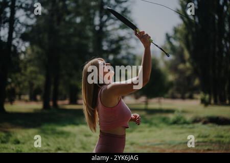 Jeune femme jouant au badminton dans un parc ensoleillé Banque D'Images