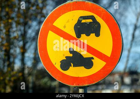 Un panneau circulaire indique que les voitures et les motos sont interdites dans la zone. Les couleurs vives se distinguent sur un ciel clair et les arbres voisins Banque D'Images