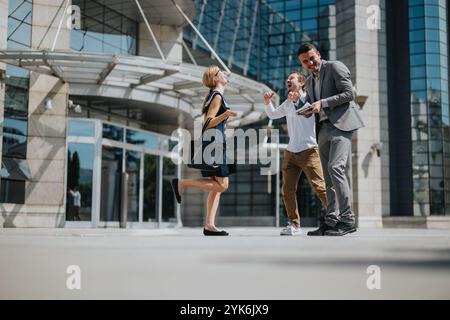 Groupe de gens d'affaires heureux célébrant à l'extérieur d'un immeuble de bureaux moderne sous le soleil, exprimant la joie et le succès après une entreprise prospère Banque D'Images