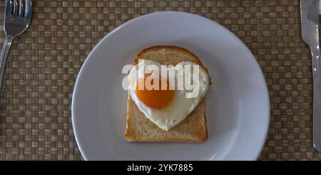 Oeuf en forme de coeur dans une tranche grillée de pain de seigle sur une plaque en céramique blanche. Concept de la Saint-Valentin. Banque D'Images