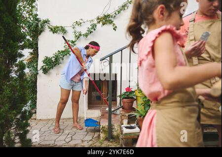 Une famille aime une journée d'été jardiner ensemble. Les enfants aident à planter pendant qu'un adulte nettoie. La scène capture le travail d'équipe, les activités en plein air Banque D'Images