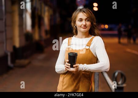 Une jeune femme appréciant une boisson chaude dans une rue calme de nuit. Banque D'Images