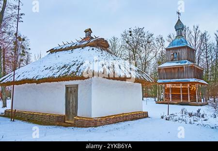 La petite maison de prêtre du village avec beffroi médiéval en bois de l'église en arrière-plan, Pereiaslav Scansen, Ukraine Banque D'Images