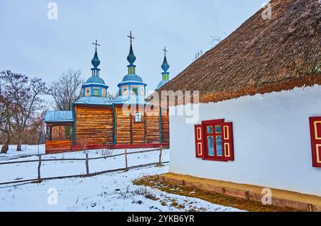 L'église historique en bois et petite maison blanchie à la chaux hata avec toit de chaume en hiver Scansen de Pereiaslav, Ukraine Banque D'Images