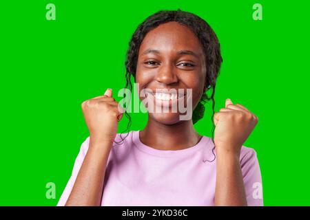 Une jeune femme avec des tresses exprime l'excitation avec un poing serré sur un fond vert vif Banque D'Images