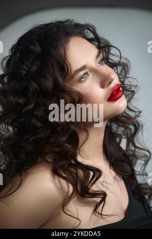 jeune femme aux cheveux bouclés succulents et aux lèvres rouges frappantes pose sans expression. Banque D'Images