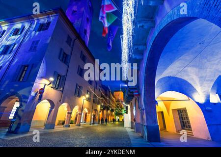 Vue en bas angle de la rue pavée étroite du soir parmi les bâtiments historiques illuminés avec des lumières de Noël à Alba, en Italie. Banque D'Images