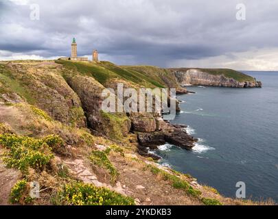 A Cap Fréhel en Bretagne, France - phare se dresse sur une colline rocheuse sous un ciel nuageux, entouré d'une végétation clairsemée et d'herbe. Banque D'Images