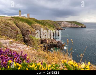 A Cap Fréhel en Bretagne, France - phare se dresse sur une colline rocheuse sous un ciel nuageux, entouré d'une végétation clairsemée et d'herbe. Banque D'Images