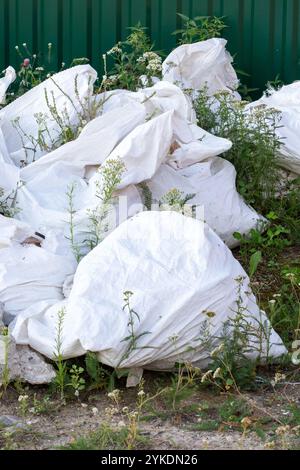 Un tas important de sacs blancs est posé sur le sol au milieu de l'herbe, créant un contraste visuel saisissant dans l'environnement naturel Banque D'Images