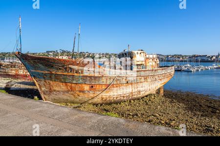 Vieux bateaux rouillés sur un rivage de Camaret sur mer en Bretagne avec un port de plaisance et des bâtiments en arrière-plan. Banque D'Images