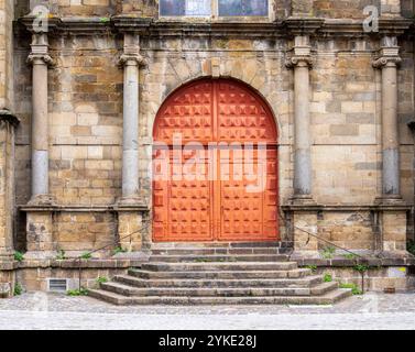 Une façade historique de bâtiment en pierre avec une grande porte en bois ornée et des marches en pierre qui y mènent. Banque D'Images