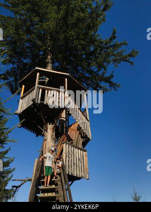 Deux enfants s'engagent dans l'aventure dans une cabane en bois rustique entourée d'une végétation luxuriante par une journée lumineuse. La scène capture l'essence de l'enfance Banque D'Images