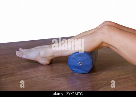 danseuse de ballet assise sur un plancher en bois massant ses mollets avec un rouleau Banque D'Images